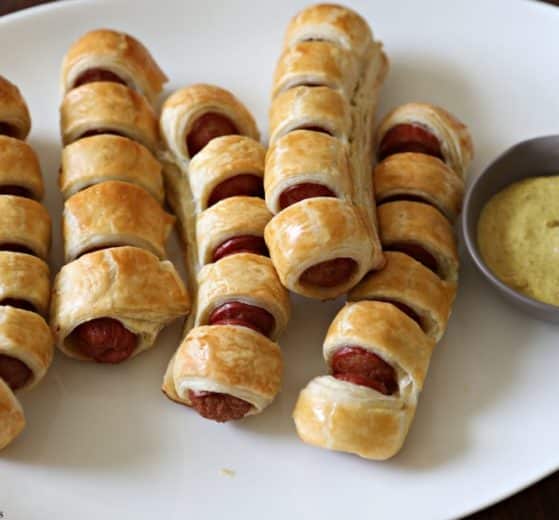 pull apart hot dogs, baked, on a white oval tray with mustard in a stainless condiment bowl