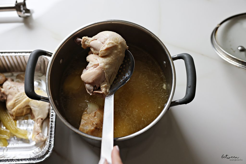 Removing celery and chicken with a slotted spoon from an 8 quart pot of broth.