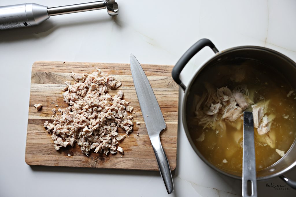 Chicken broth and chicken tops in an 8 quart pot. Chopped chicken bottoms on a wooden cutting board.