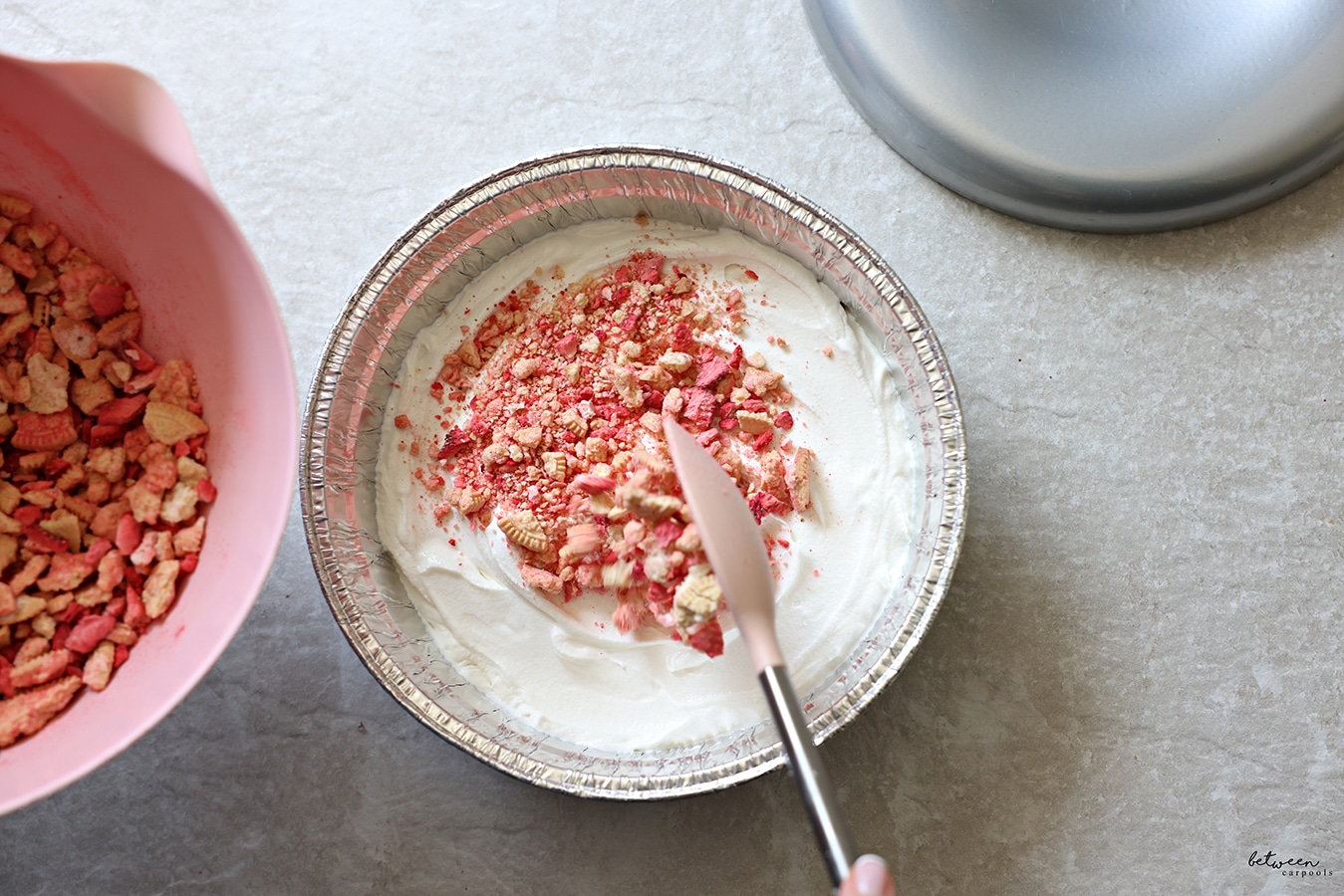 adding crunch to half of the ice cream in a round aluminum cake pan