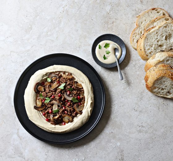 Plated chummus bassar with bread nearby.