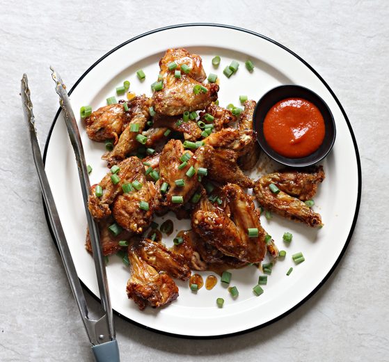 Wings, plated - topped with scallions - and hot sauce