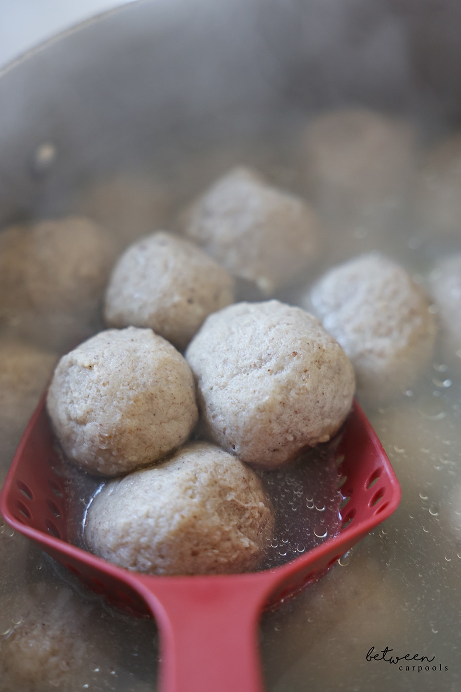Cooked Matzah balls in a pot, three in a red colander scooper.
