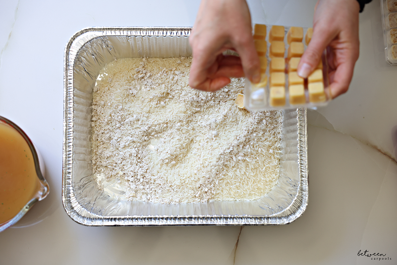 Adding frozen garlic cubes to a 9x13 baking pan with jasmine rice and onion soup mix.