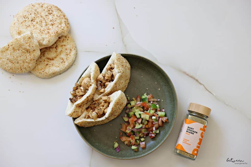 Chicken in pitas on a plate with Israeli salad. More pitas and Pinch Busy Chicken Blend nearby.