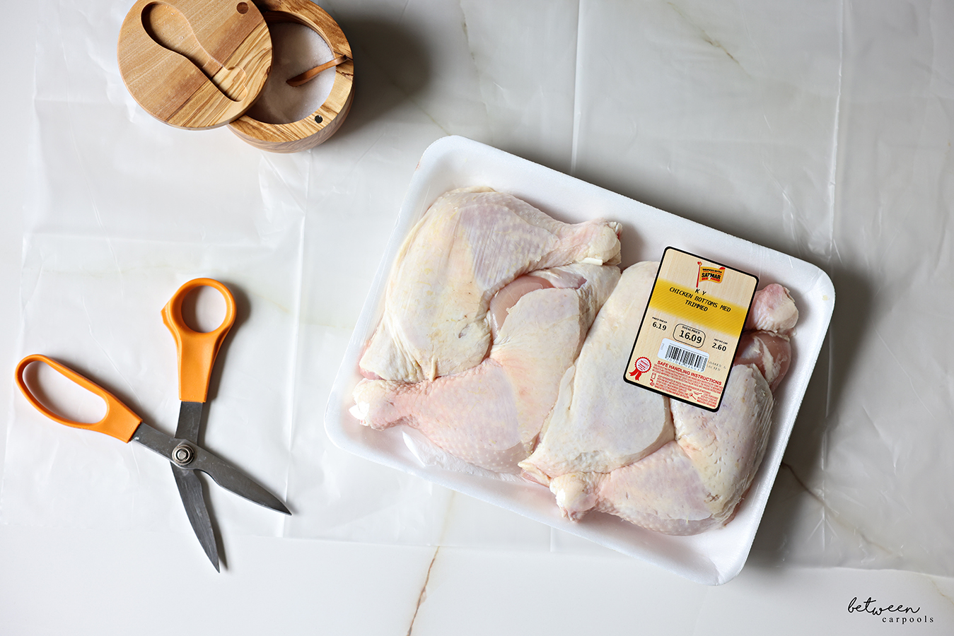 One tray packaged chicken bottoms on a counter saver. Salt cellar and chicken scissors nearby.