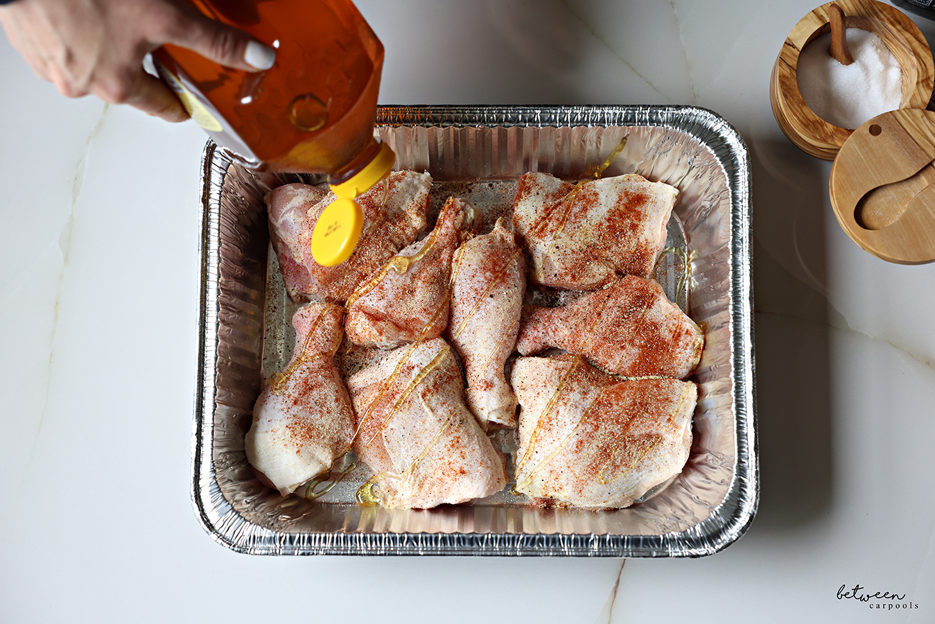 Drizzling honey over chicken bottoms in a 9 x 13 aluminum pan, sprinkled with salt, garlic powder, paprika, and pepper.