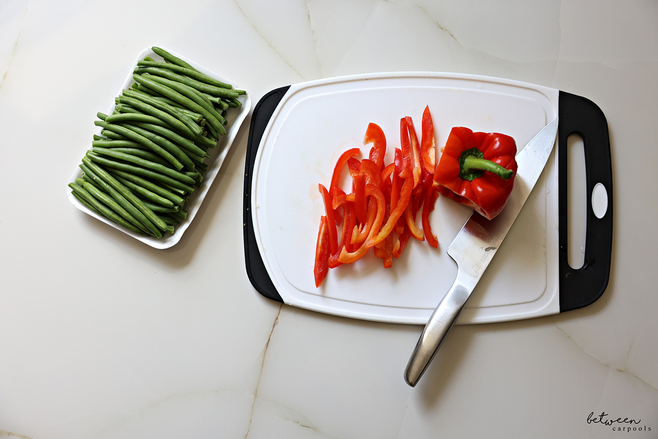 Sliced red pepper on a plastic cutting board, and a tray of French green beans.