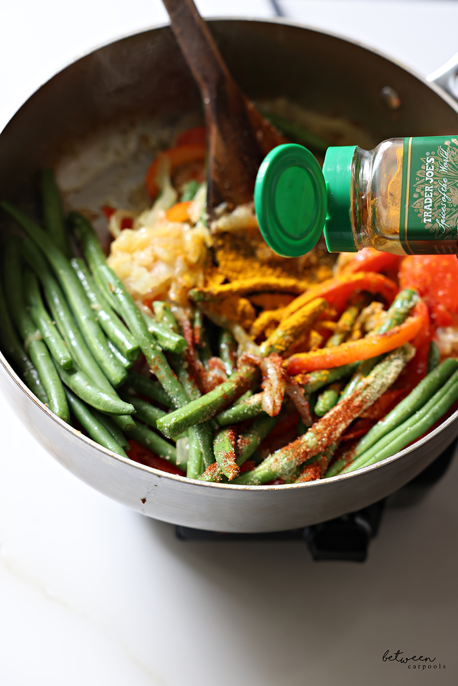 Seasoning French green beans, sautéed onion, garlic, and red pepper slices, with turmeric powder, in a sauté pan.