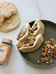 Closeup of chicken in pitas on a plate with Israeli salad. More pitas and Pinch Busy Chicken Blend nearby.