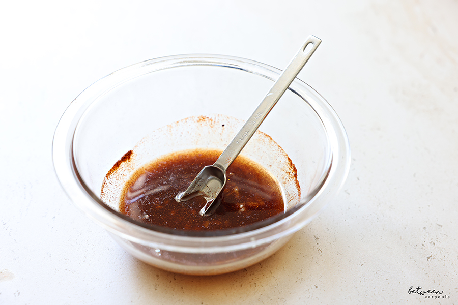 Oil, sea salt, sugar, paprika, and crushed garlic cloves, in a glass bowl with a 1 tsp. measuring spoon.