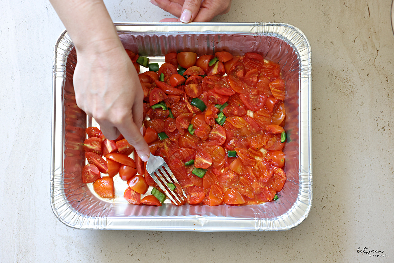 Smashing down par baked tomatoes and jalapeño, using a fork, in a 9x13 disposable baking pan.