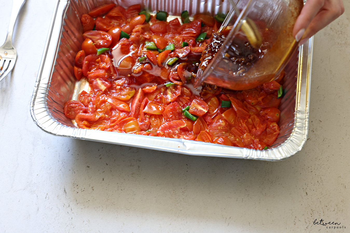 Pouring the sauce over the smashed down tomatoes and jalapeño in the 9x13 disposable baking pan.