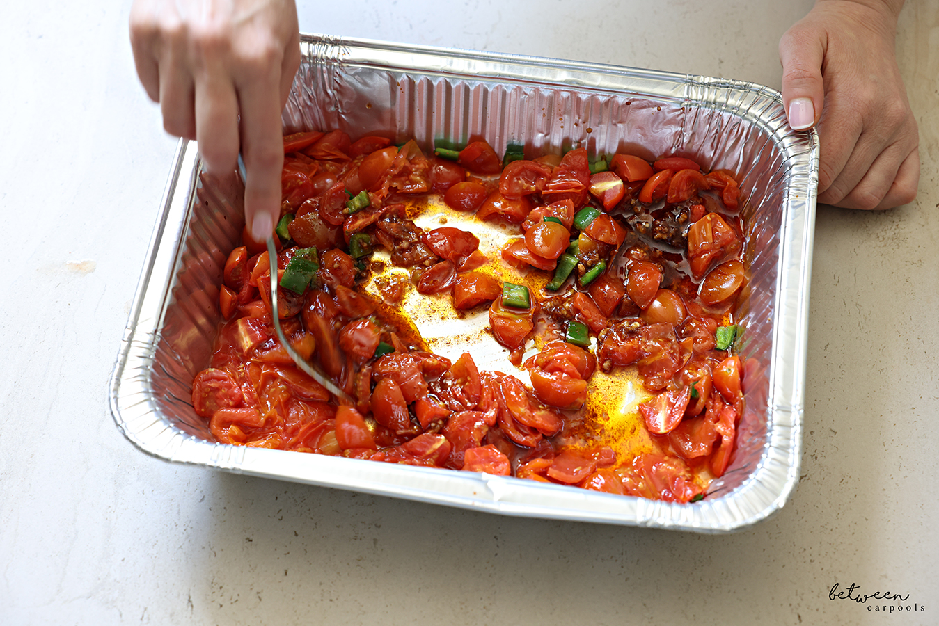 Mixing the smashed down tomatoes and jalapeño with the sauce in a 9x13 disposable baking pan.