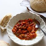 Oven matbucha in a scalloped serving bowl, sourdough nearby.