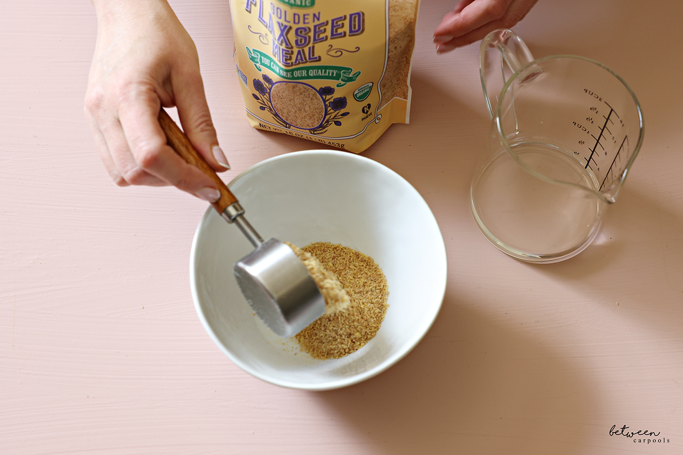 Pouring flaxseed meal into a small white bowl. Bag of flaxseed meal and a glass measuring cup nearby.