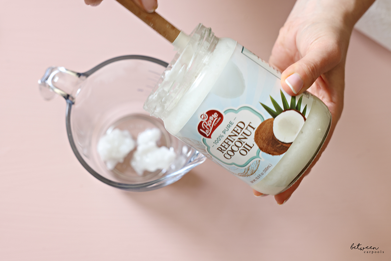 Measuring coconut oil into a glass measuring cup with a spatula.