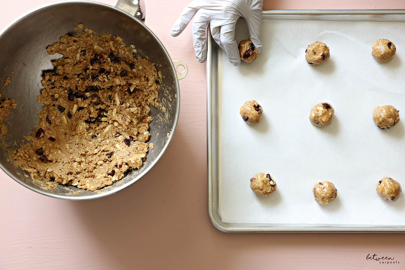 Placing rolled balls of small bits of cookie dough on a parchment lined baking sheet. Lactation cookies dough in the bowl of an electric mixer nearby.