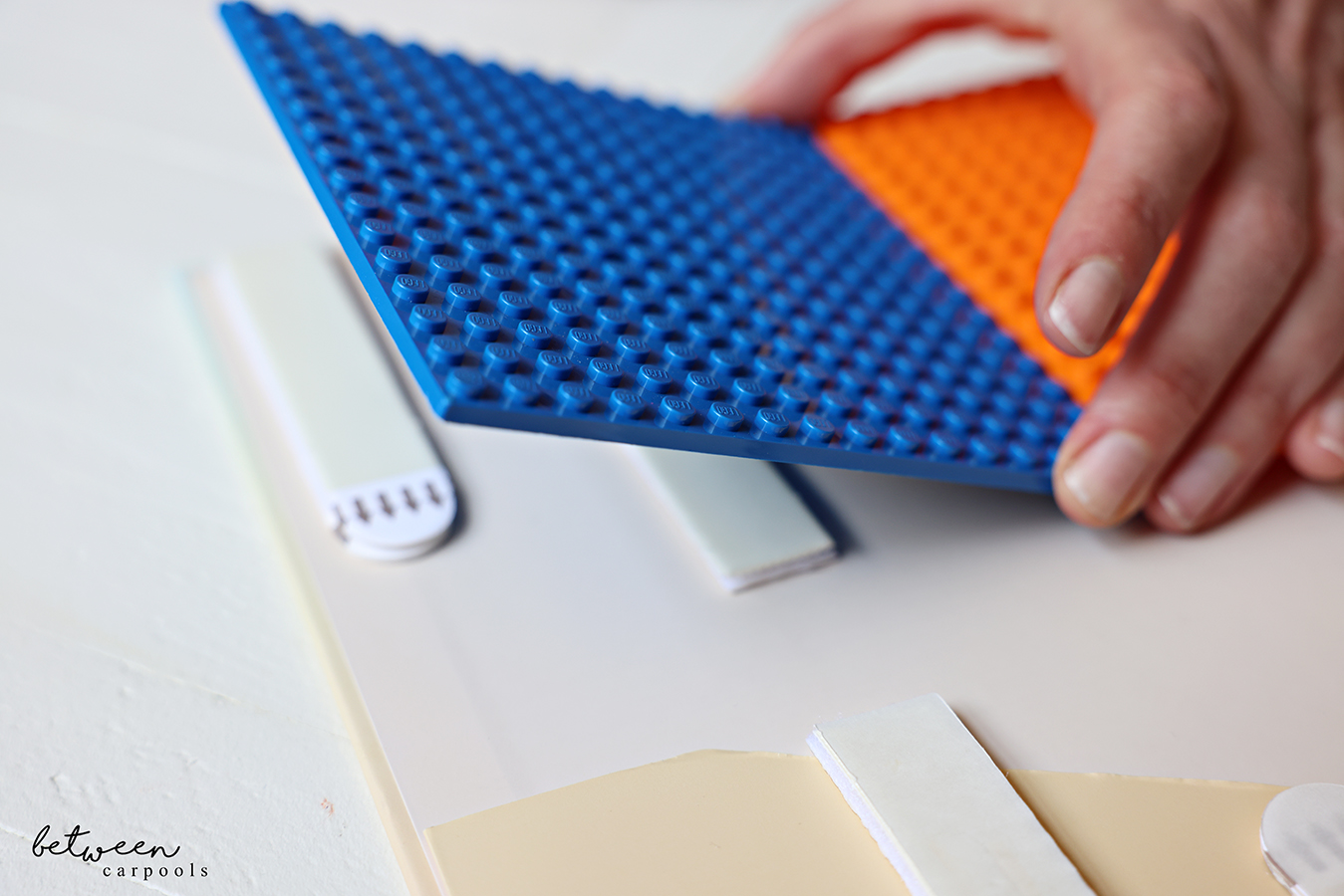 Sticking small Lego plates onto picture hanging strips on the inside back cover of a hardcover binder.