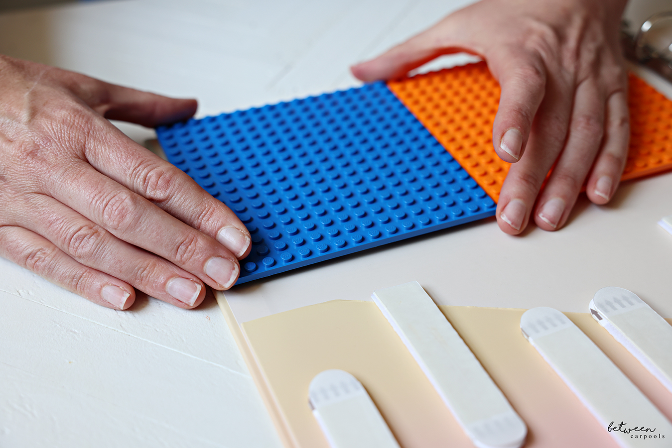 Small Lego plates attached to picture hanging strips on the inside back cover of a hardcover binder.