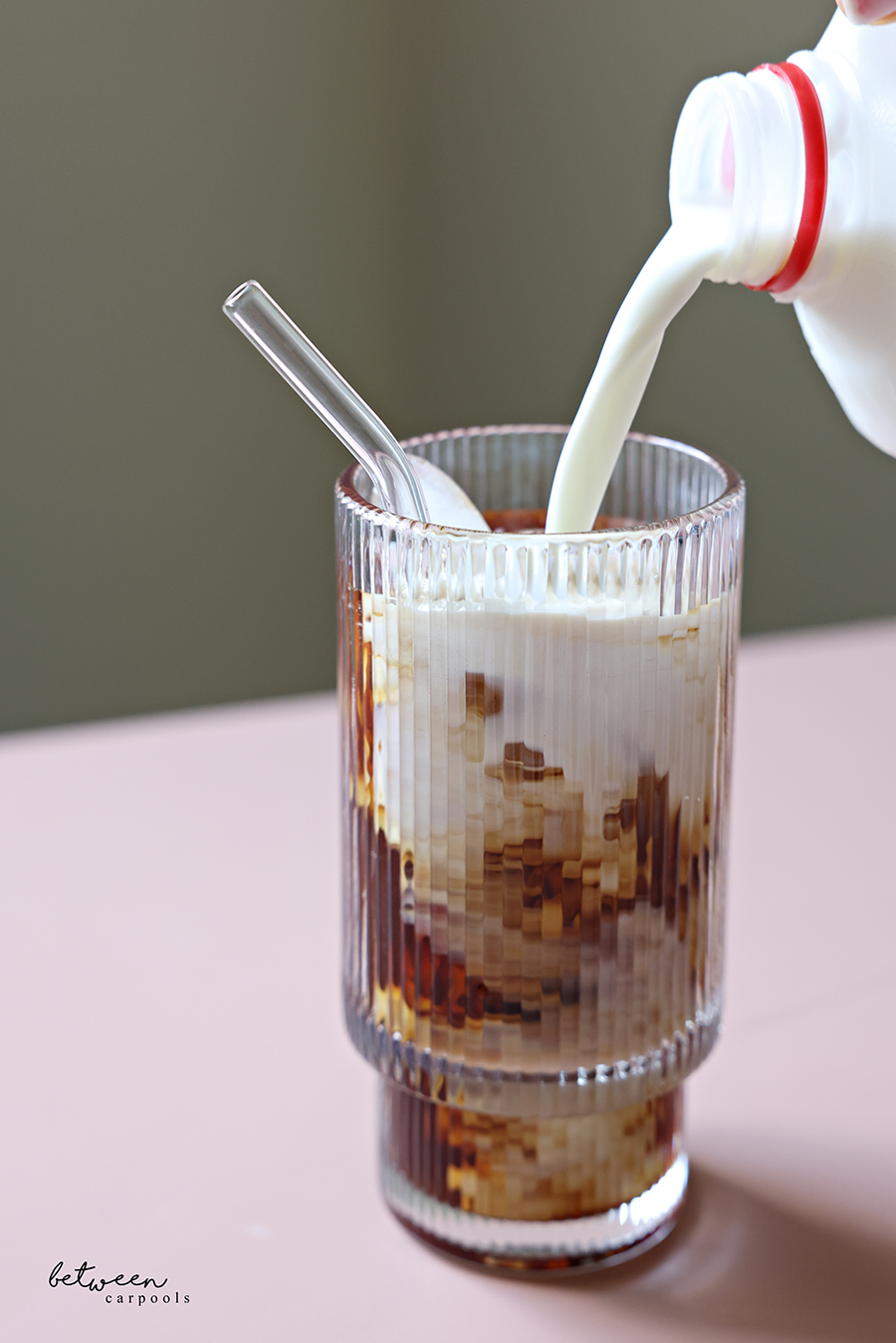 Pouring milk into a glass with cold brew over ice.
