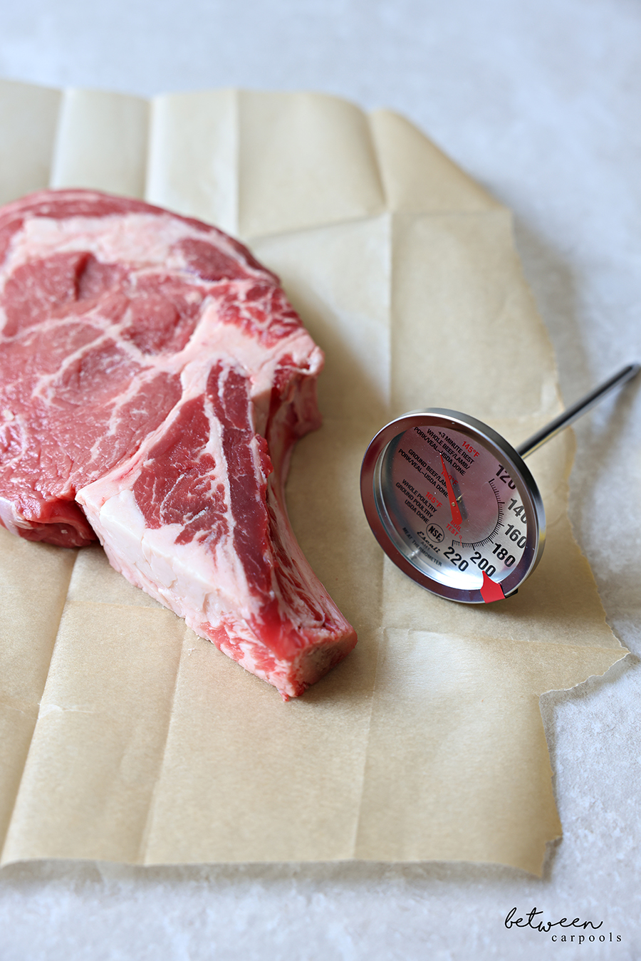 An Escali Stainless Steel Oven Safe Meat Thermometer near a bone-in ribeye on a piece of natural parchment paper.