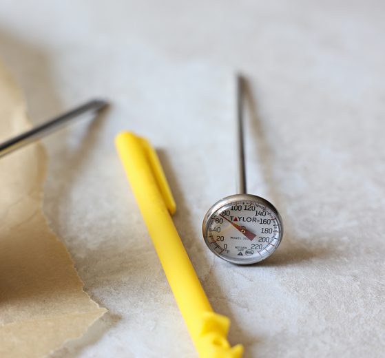 Taylor Instant Read Meat Thermometer with Red Pocket Sleeve near a piece of natural parchment paper.