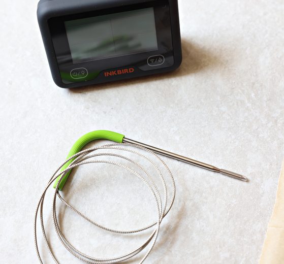 Inkbird Bluetooth/WiFi Meat Thermometer with a green probe near a piece of natural parchment paper.