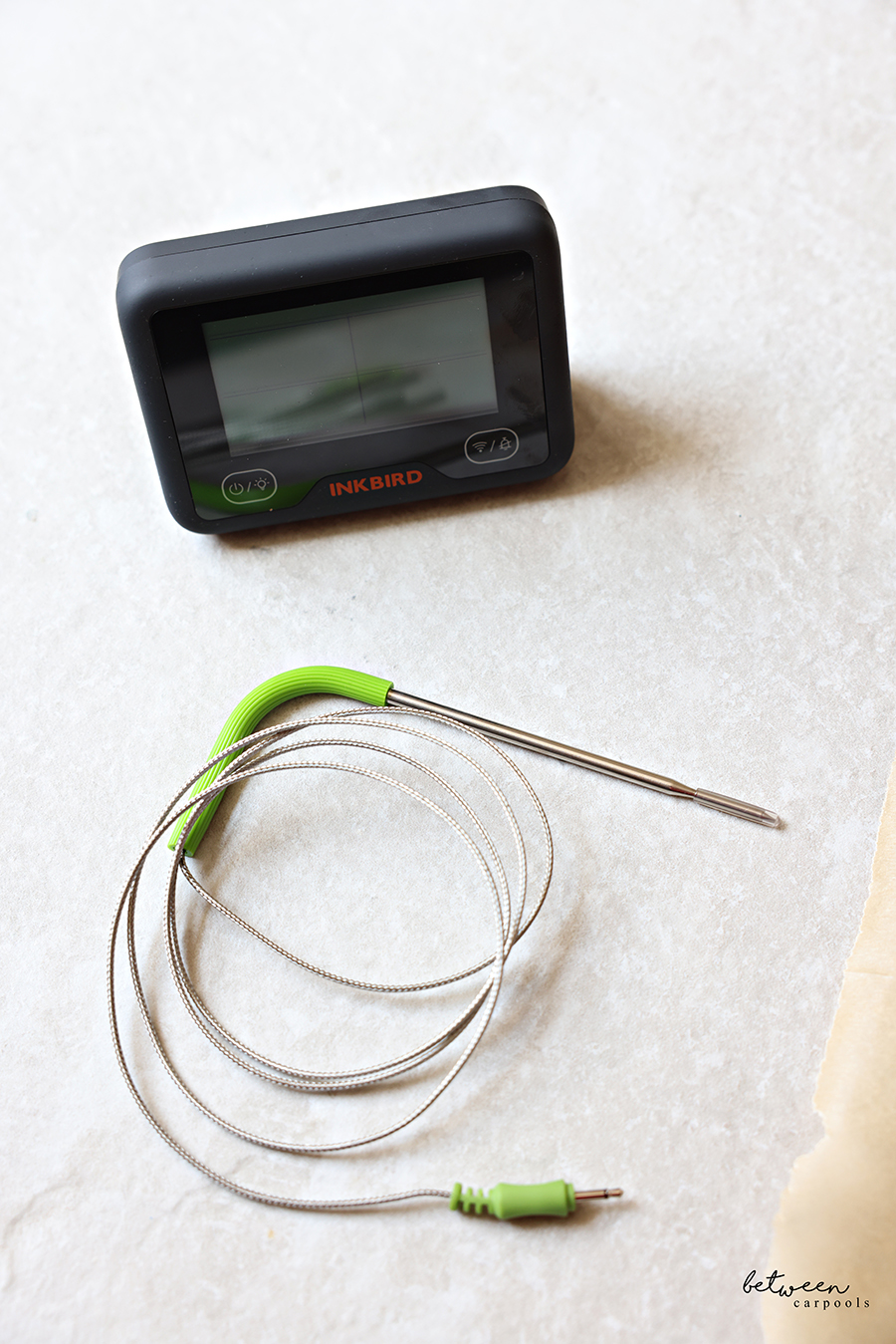 Inkbird Bluetooth/WiFi Meat Thermometer with a green probe near a piece of natural parchment paper.