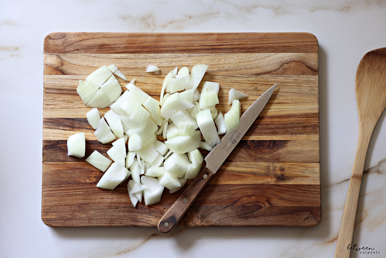 Large chunks of onion on a wooden cutting board with an Icel knife wood handle. Wooden paddle nearby.
