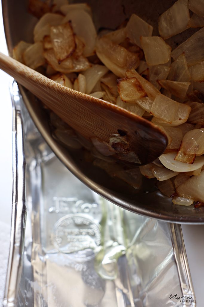 Draining the oil from sautéed onion in a sauté pan into an aluminum loaf pan with a wooden paddle.