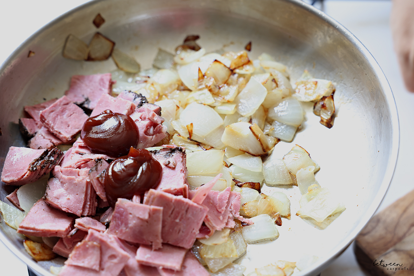 Cubed deli pastrami and 2 tbsp BBQ sauce added to sautéed onion chunks in a sauté pan.