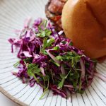Red Cabbage Salad with Sumac near a burger topped with pastrami topping in a bun on a plate.