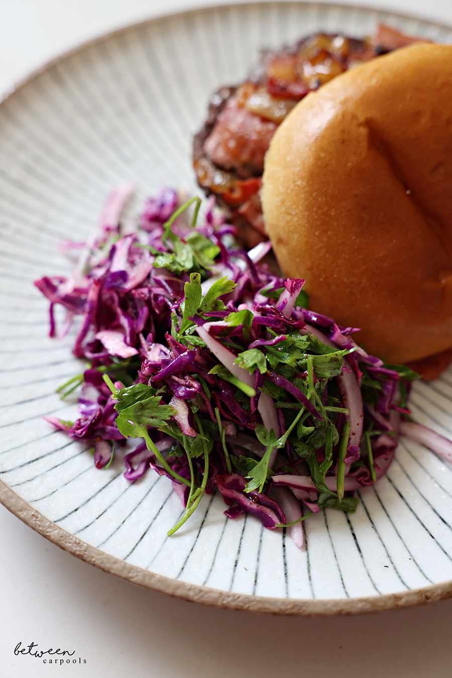 Red Cabbage Salad with Sumac near a burger topped with pastrami topping in a bun on a plate.