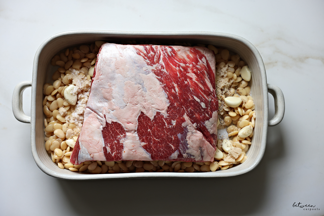 Flanken roast on top of boiled lima beans, whole garlic cloves and spices, in a roasting pan.