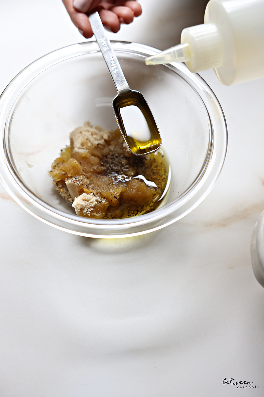 Adding olive oil to a glass bowl with rub ingredients for flanken roast over lima beans.