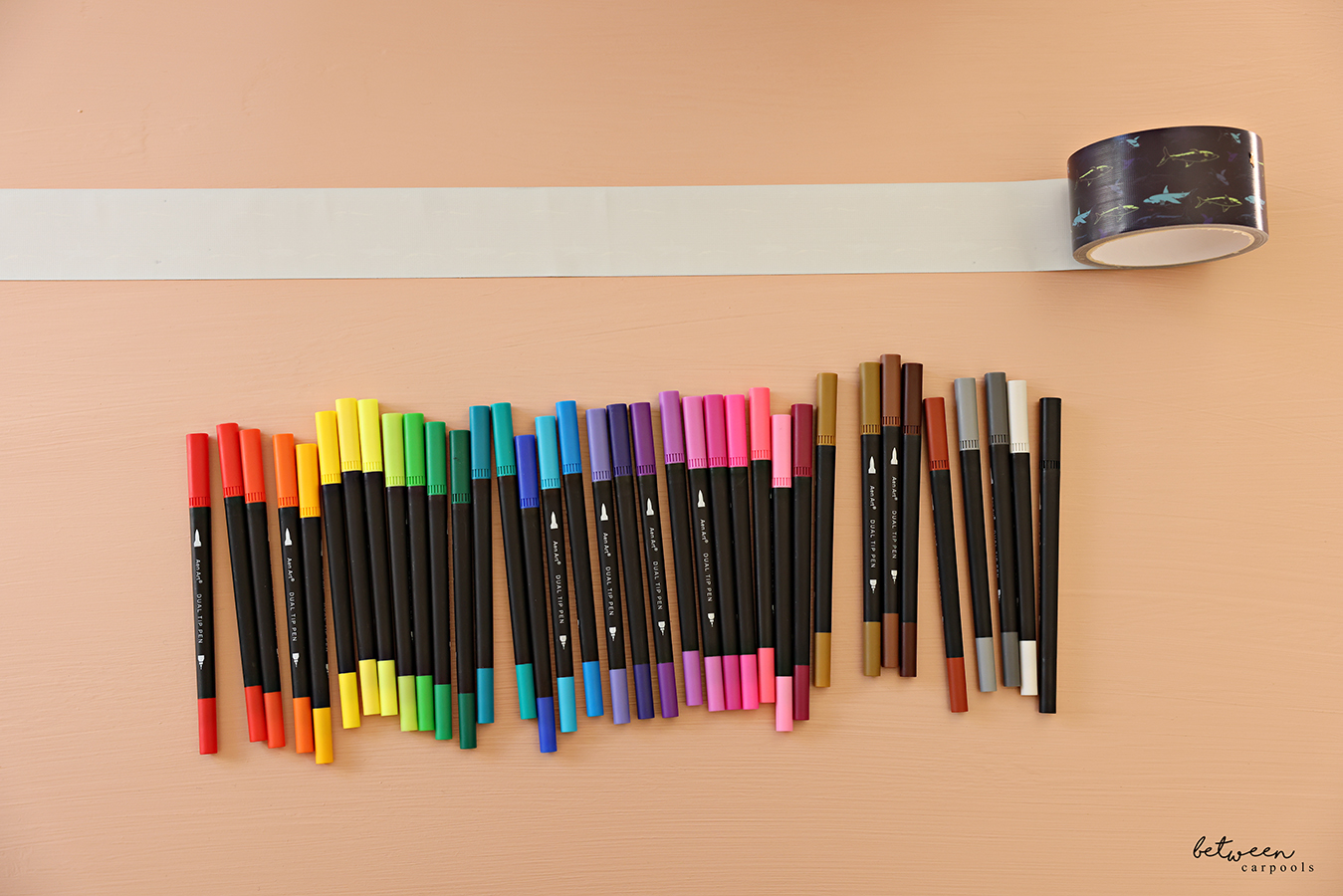 Unrolled duct tape, sticky side up, above markers lined up by shade.