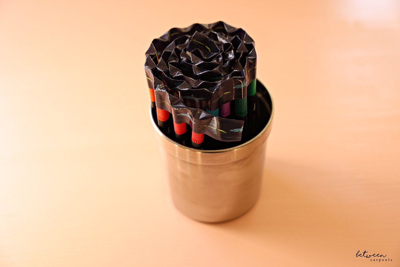 A set of markers with its caps held together with duct tape, in a pencil cup.