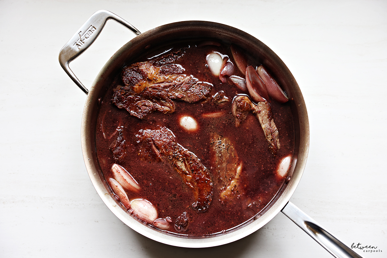 Seared boneless flanken in a pot with sautéed shallots, seasoning, and liquid.