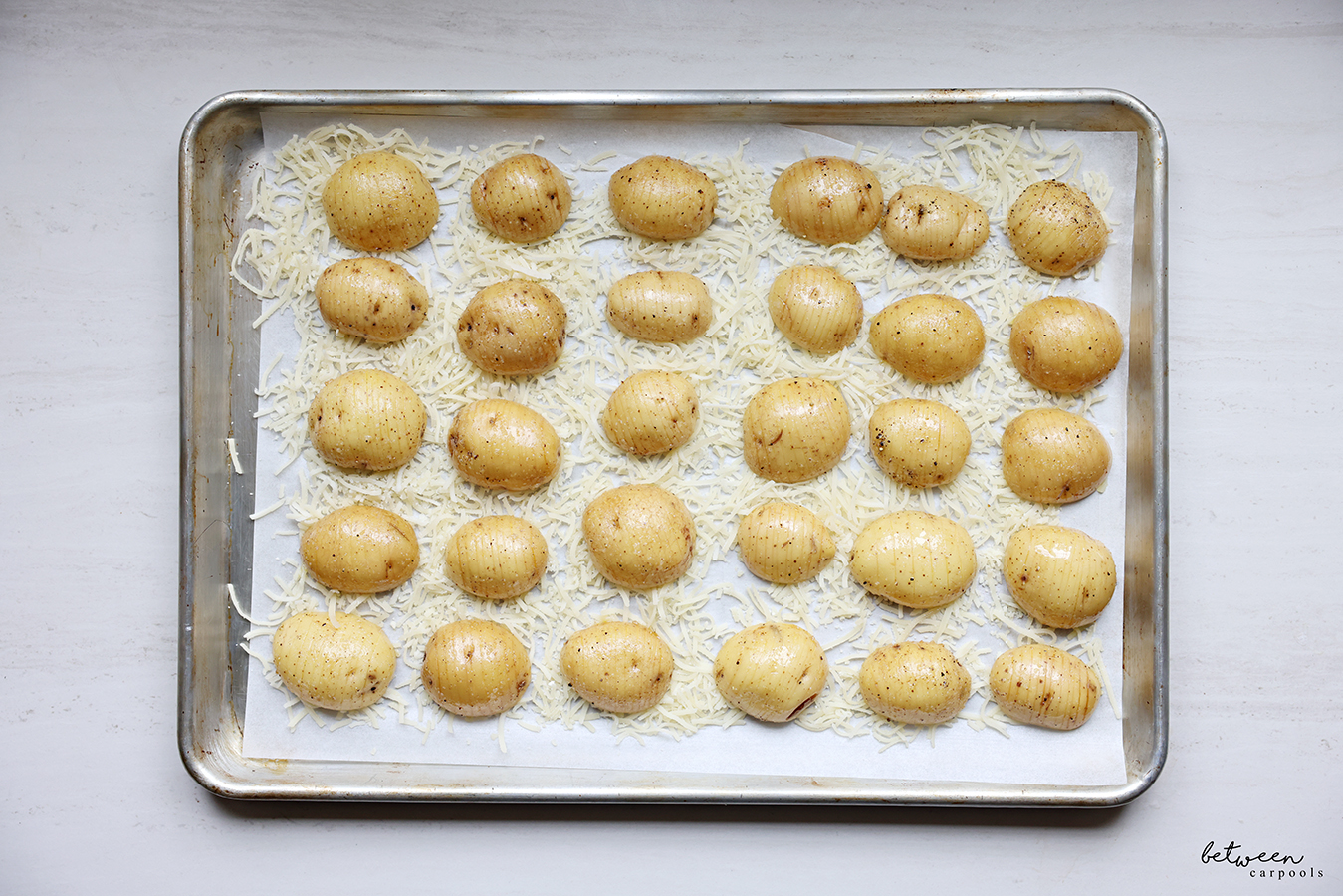 Hasselback baby potato halves lined up on Parmesan cheese on a parchment lined sheet pan.