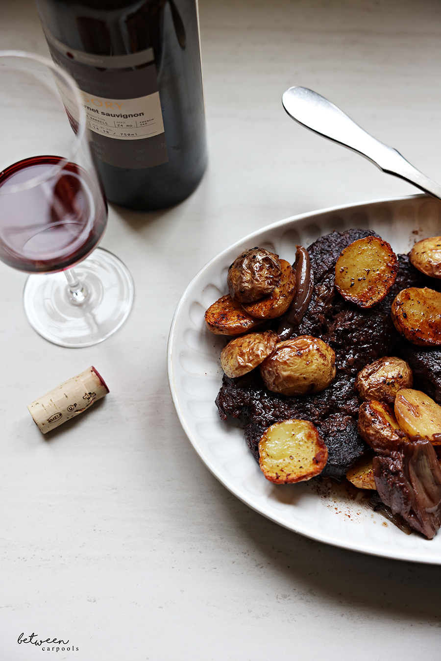 Boneless flanken and potatoes with shallots and red wine, on a serving platter. Glass of cabernet sauvignon nearby.