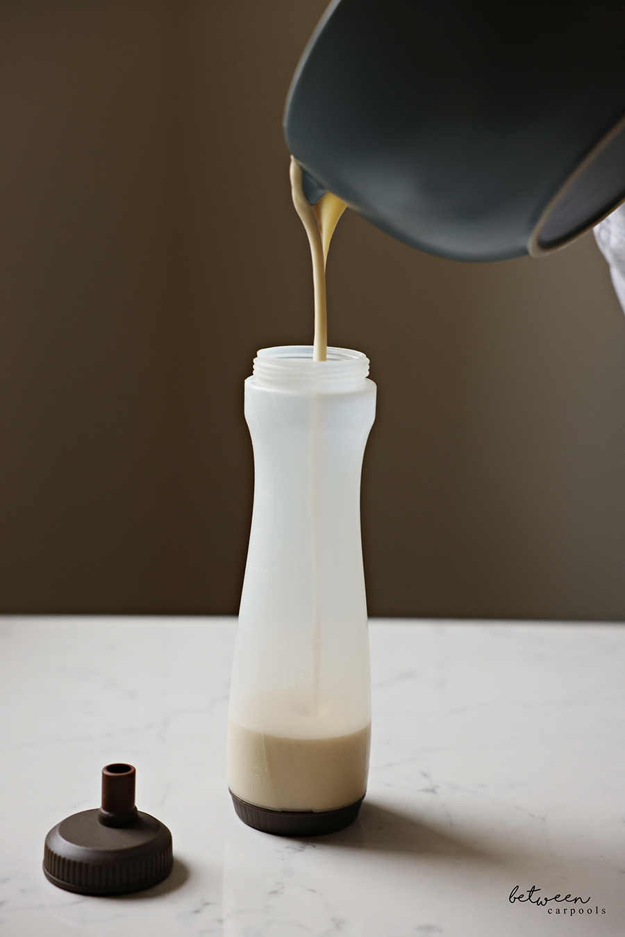 Pouring pancake batter from a large spouted bowl into a pancake squeeze bottle.