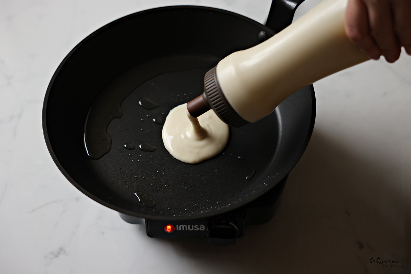 Squeezing some batter from a pancake squeeze bottle into a frying pan.