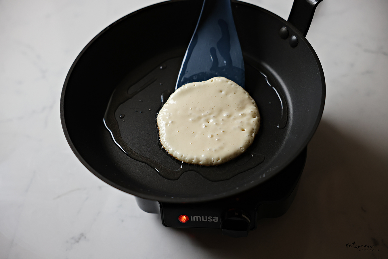 Lifting a pancake, with bubbles on its surface, in a frying pan with a spatula.