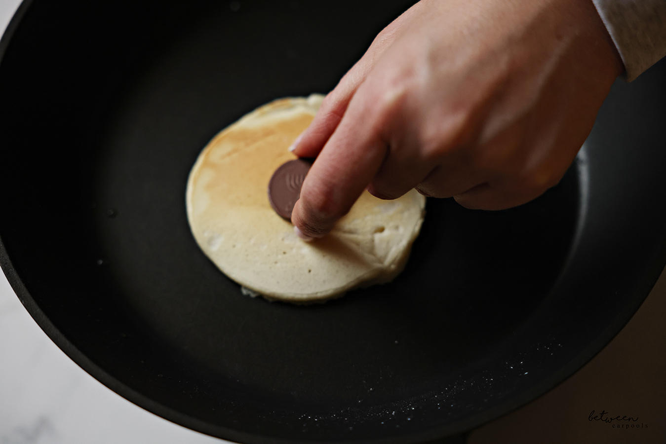 Adding a Chanukah gelt to the center of a flipped pancake in a frying pan.