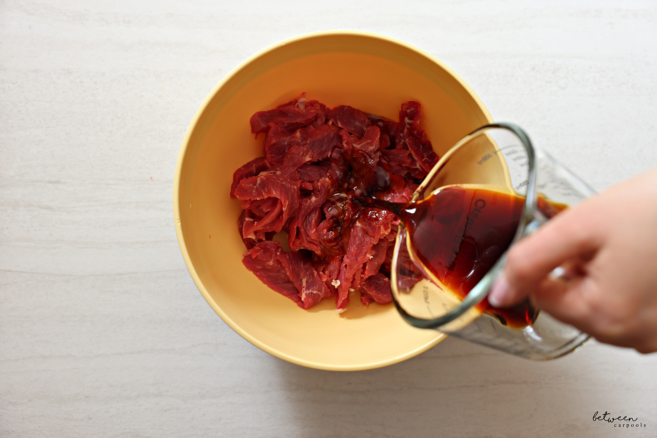 Pouring marinade over thinly sliced steak in a mixing bowl.