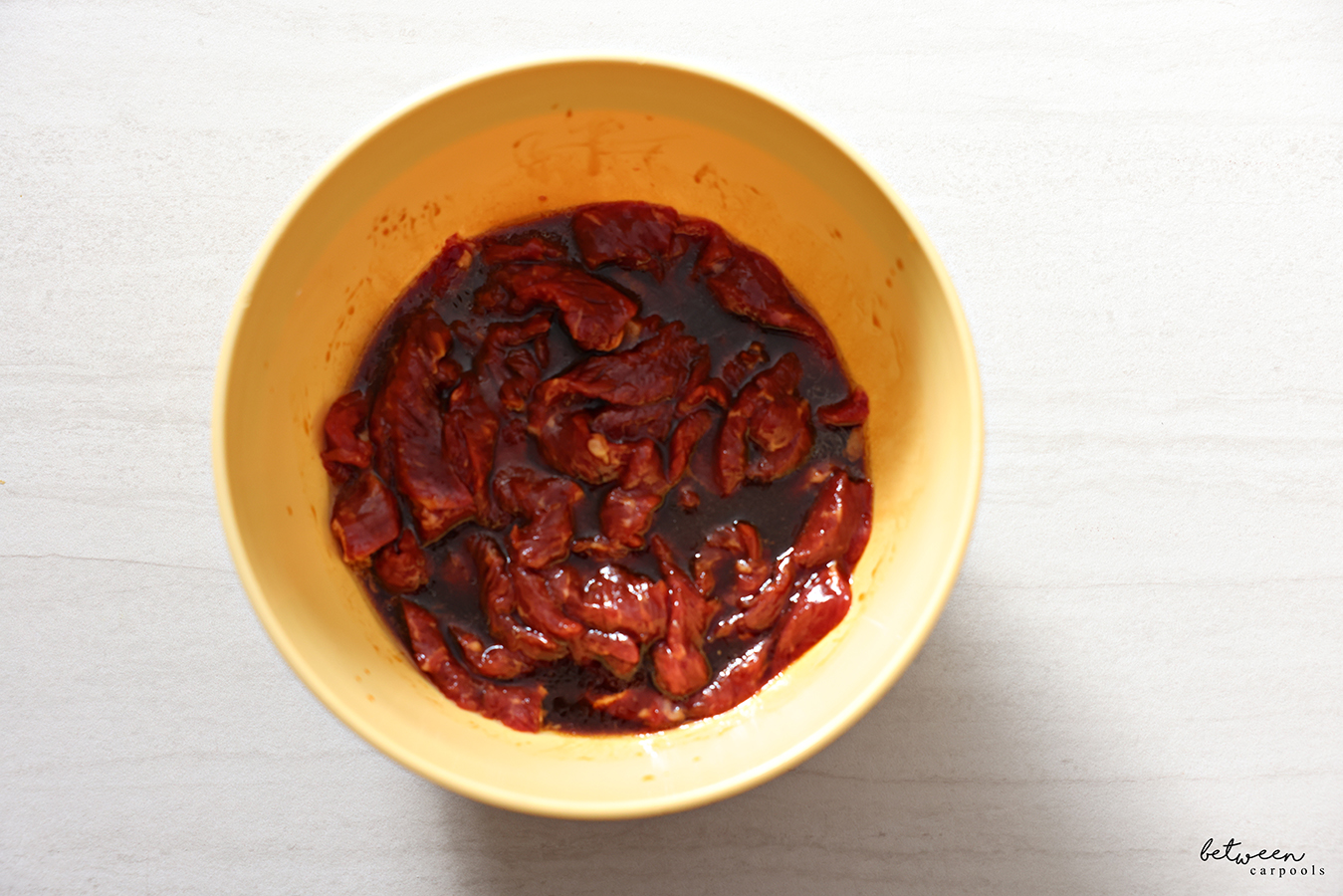 Thinly sliced steak and marinade marinating in a mixing bowl.