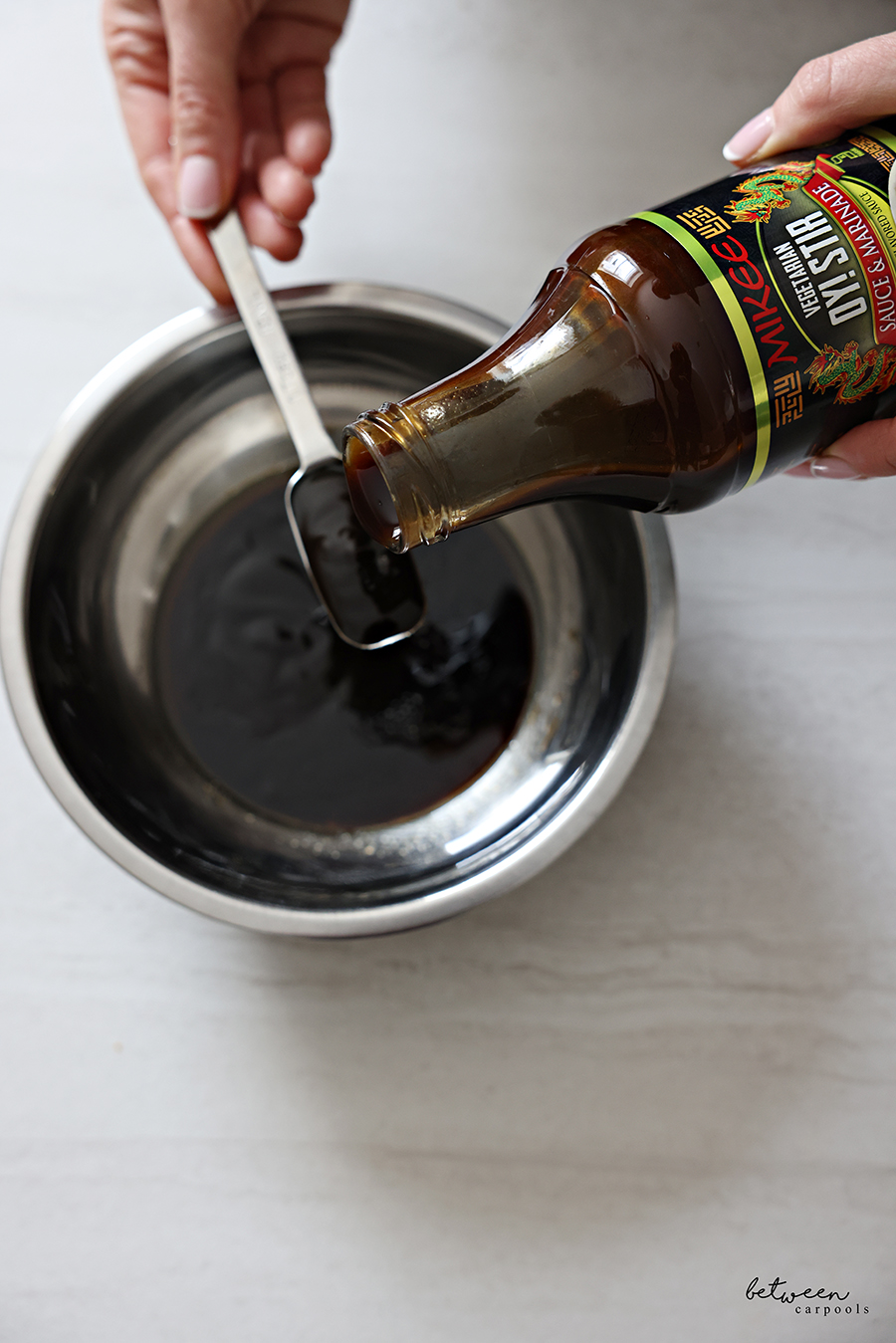 Measuring Mikee Oyster Sauce over a small stainless mixing bowl.