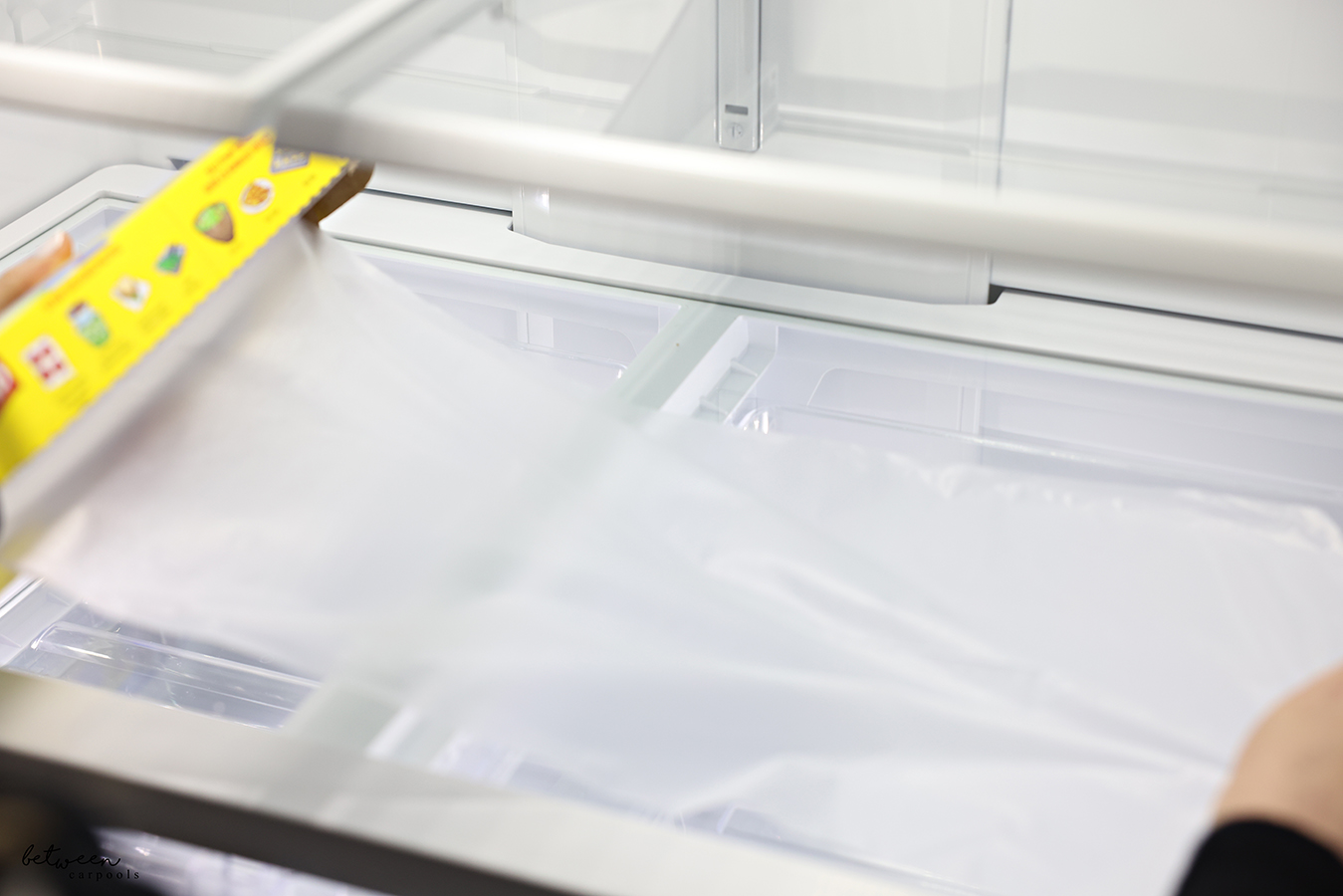 Pulling plastic food wrap from the roll of Glad Press n' Seal on a clean fridge shelf.