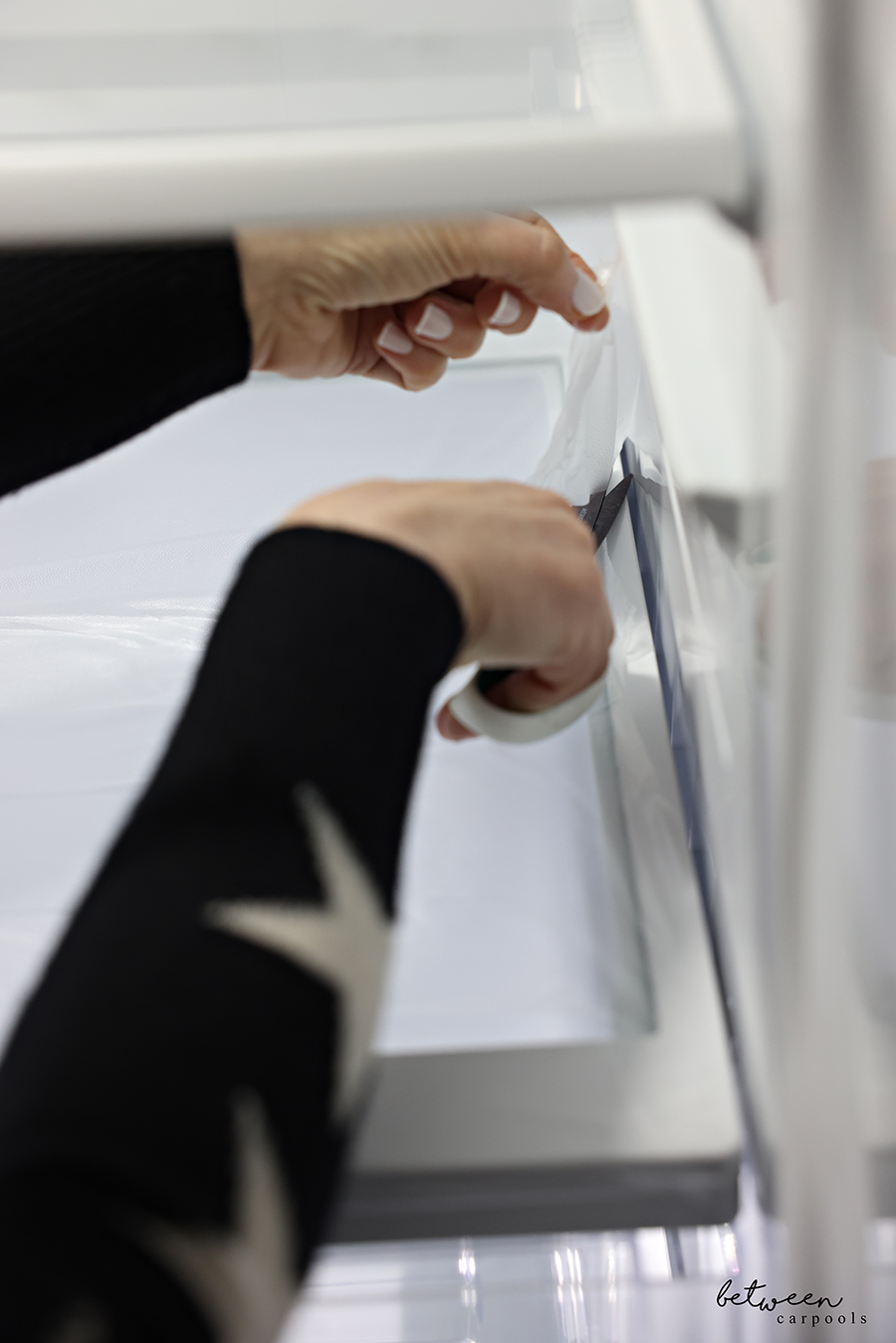 Trimming the excess of Glad Press n' Seal pressed down on the plastic frame of a clean fridge shelf.